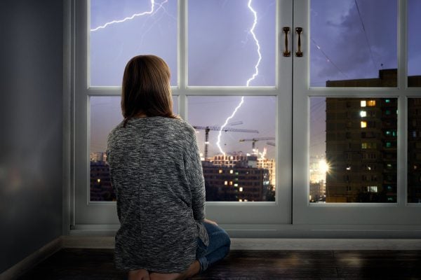 The girl looks through the window at the lightning. Thunderstorm in the city